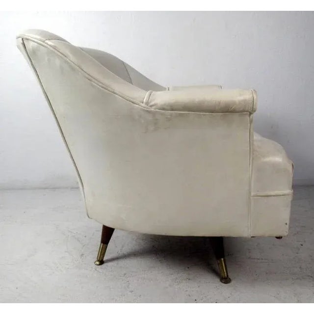 This midcentury lounge chair features a white scalloped back vinyl seat and swivel base on tapered legs which offer a...
