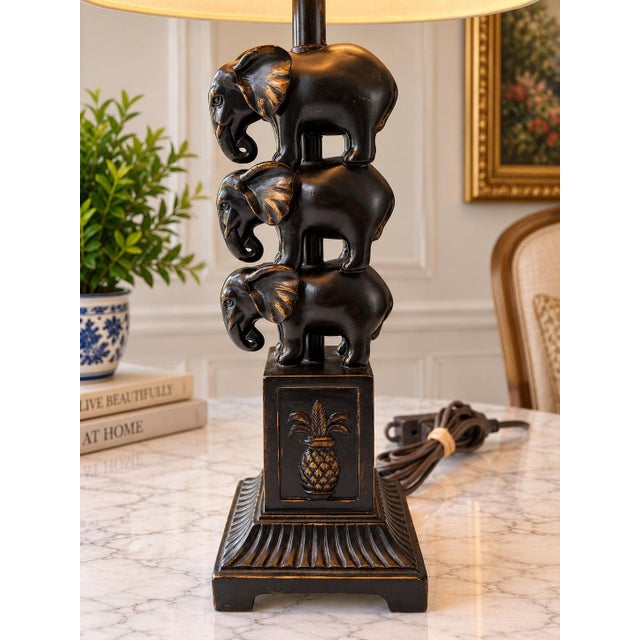 Striking vintage table lamp featuring a sculptural trio of elephants in a stacked design, finished in black with warm gold...