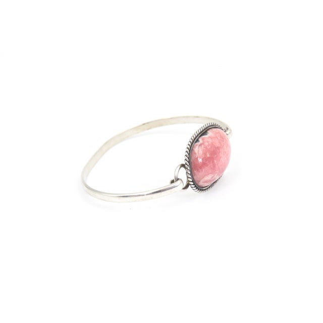 Silver bangle bracelet with an oval cabochon rhodochrosite in the center of a twisted rope frame. Opens with a hook clasp....