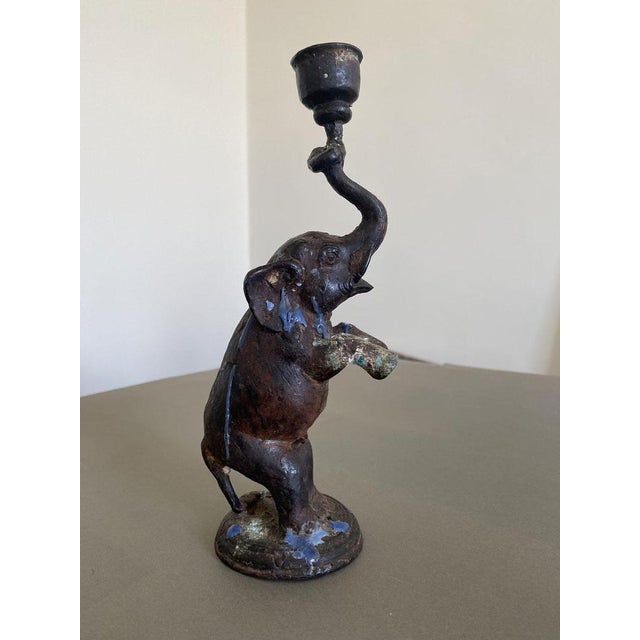 The bronze sculpture depicts an elephant standing on its hind legs to raise a candle holder. The artifact is of Eastern...