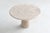 This sculptural dining table features a beautifully honed round travertine top with rich natural patterning in warm cream...