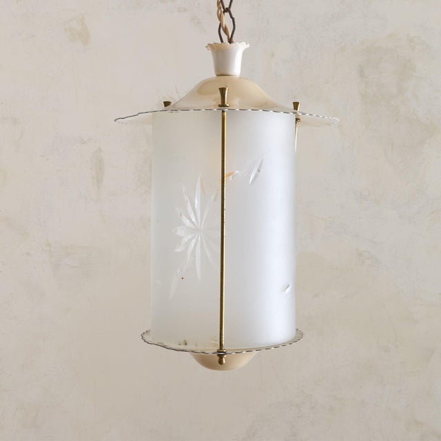 A 1950s Italian lacquered metal lantern pendant with a cylindrical silhouette. The ivory-toned frame descends from a...