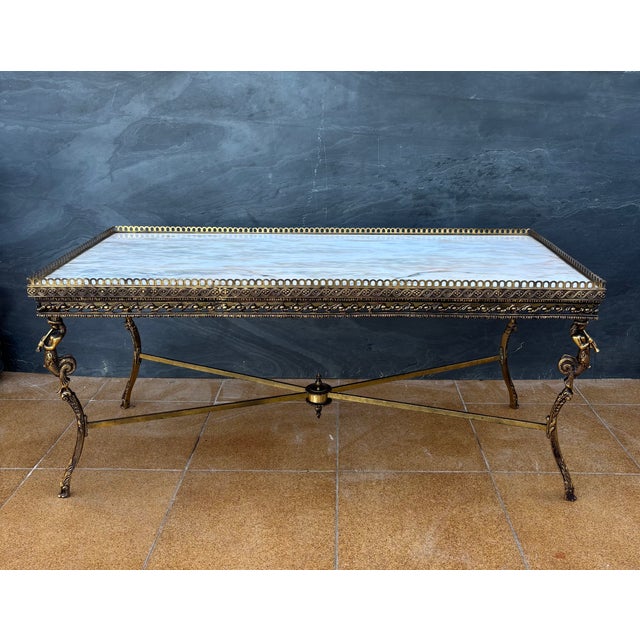 Elegant neoclassical style coffee table featuring a marble top and a finely crafted gilt metal structure. The table stands...