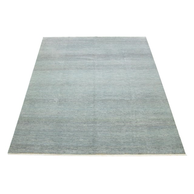 This elegant hand-knotted wool rug features a contemporary design. It showcases a meticulously crafted field in light...