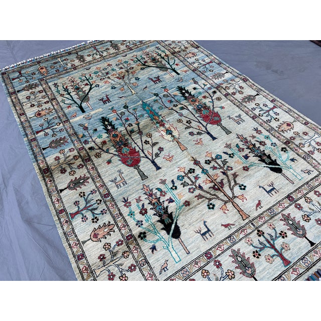This hand-knotted Afghan pictorial rug depicts tiered rows of stylized cypress and flowering trees populated with deer,...