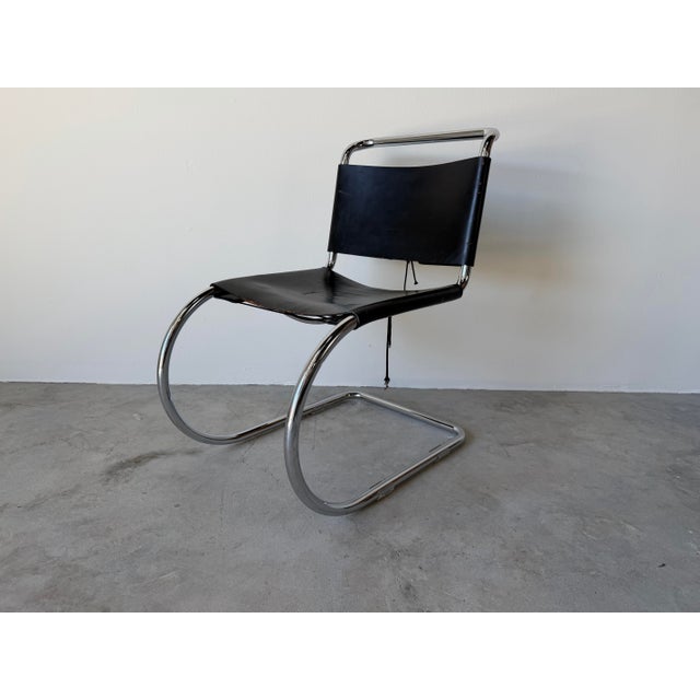 Iconic 1960s Mies van der Rohe–style cantilever chair featuring a sleek tubular chrome frame paired with a black leather...