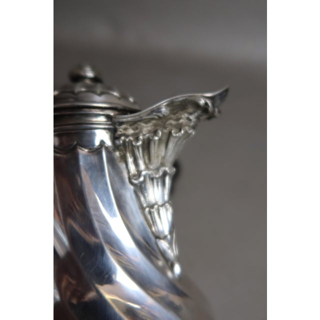 A solid silver coffee pot resting on three hoof-shaped feet with cartouche-shaped brackets decorated with flowers and...