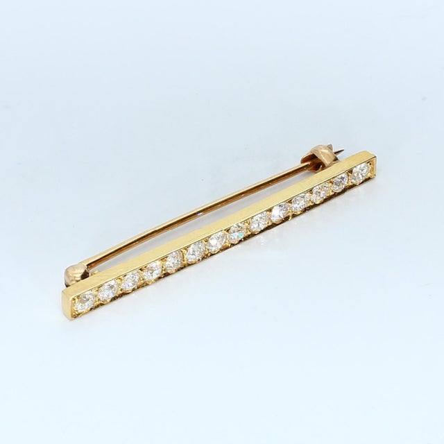 This bar brooch features a row of twelve white diamonds set in yellow gold. Stone Info: 12x Diamonds SI2/E ~0.06ct/ea...