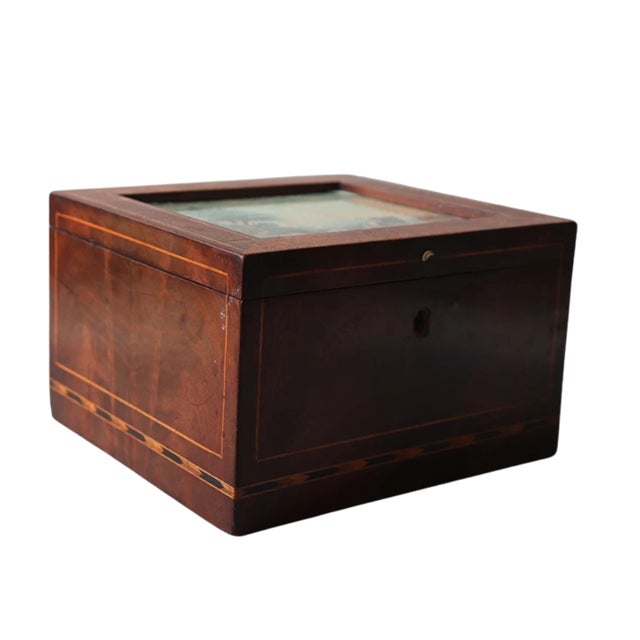 An antique British Victorian wooden tea caddy featuring a painted pastoral scene with figures and livestock, framed by...