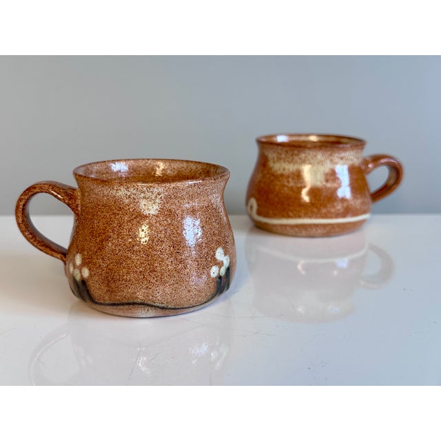 Two handcrafted ceramic mugs by Helma Klett, each with a workshop signature on the underside. Different designs in warm...