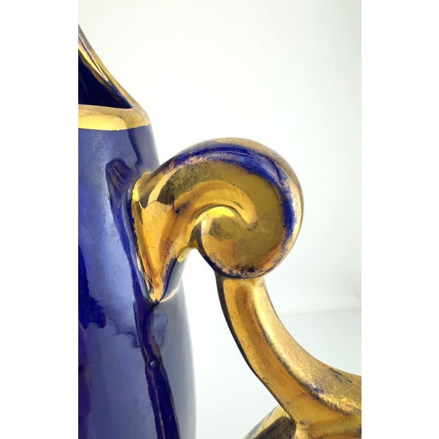 A sculptural mid-century art pottery pitcher featuring a rich cobalt blue glaze accented with hand-applied gilt detailing...