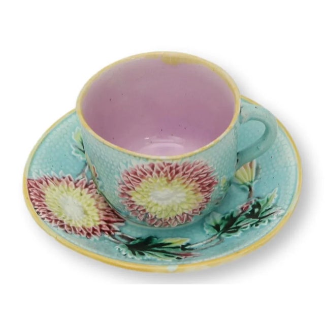 A rare antique majolica cup and saucer, richly molded with bold chrysanthemum blossoms in vibrant turquoise, rose, and...