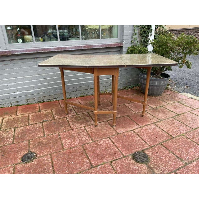 This is a vintage mid-century drop-leaf table, commonly used in kitchens or small dining areas for its space-saving...