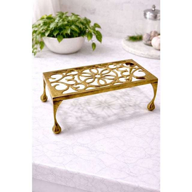 Vintage solid brass trivet stand with intricate pierced scrollwork and a raised footed silhouette, offering both function...