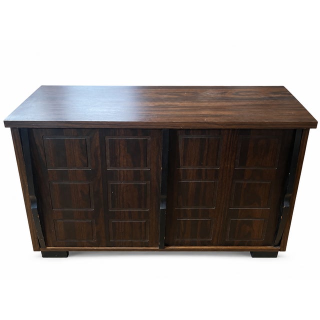 This is a vintage 1970s Mid Century modern dark wooden fold out wooden dry bar cabinet. This cabinet features a geometric...