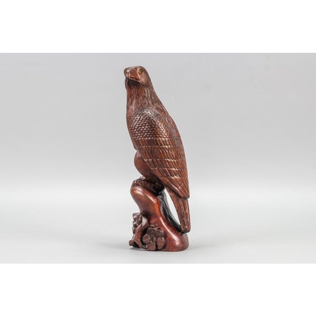 This stunning, naturalistically hand carved and brown tinted beechwood eagle figure with glass eyes, perched on a wooden...