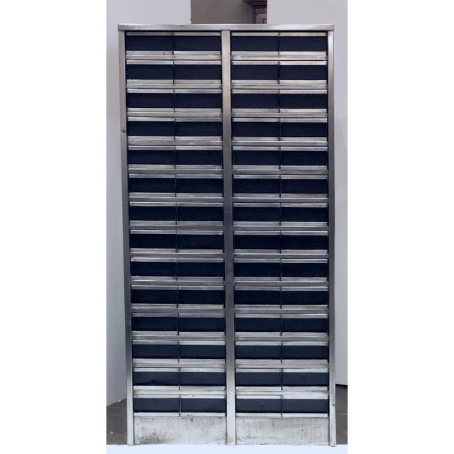 A fine large English industrial cabinet of burnished steel featuring (56) small half-drawers for storage, set into four...