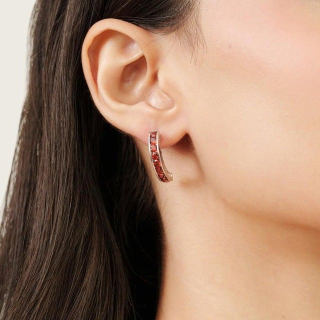 Radiating timeless elegance, these refined half hoop earrings showcase a graceful arc of vibrant garnet totalling...
