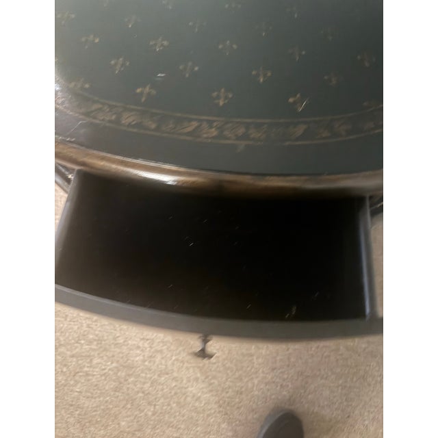 Elegant Hollywood Regency–style demi-lune accent table featuring a black painted finish with subtle gilt stencil detailing...