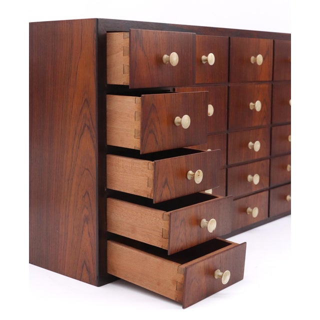 1960s Mid Century rosewood wall cabinet with twenty drawers in a four across, five down arrangement. There are inset...