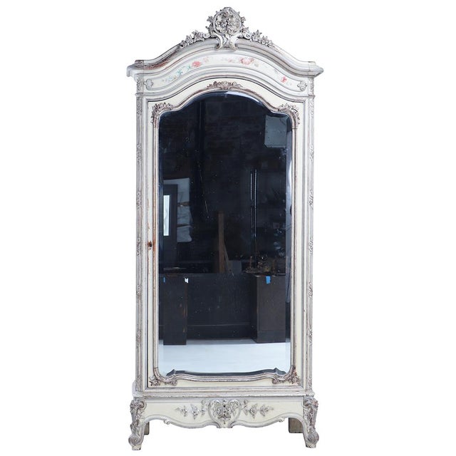 A charming French floral painted walnut armoire, C. 1880, featuring an elaborately carved architectural form and delicate...