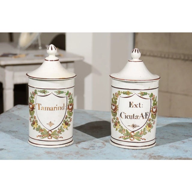 A pair of French Directoire period ceramic lidded apothecary jars from the late 18th century, with hand-painted foliage...