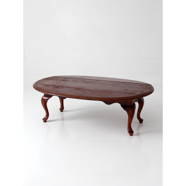 Vintage Queen Anne style drop leaf coffee table with elongated oval form, cabriole legs, and carved shell details at the...