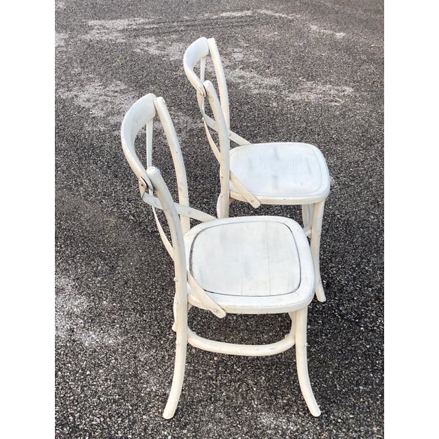 Two distressed white washed chairs by Palecek. Chairs have a nice bentwood foot rail.