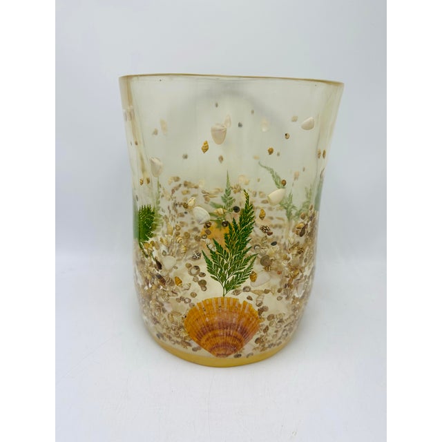 A vintage lucite/resin wastebasket with a seaside theme. The translucent amber-toned body is embedded with real seashells,...