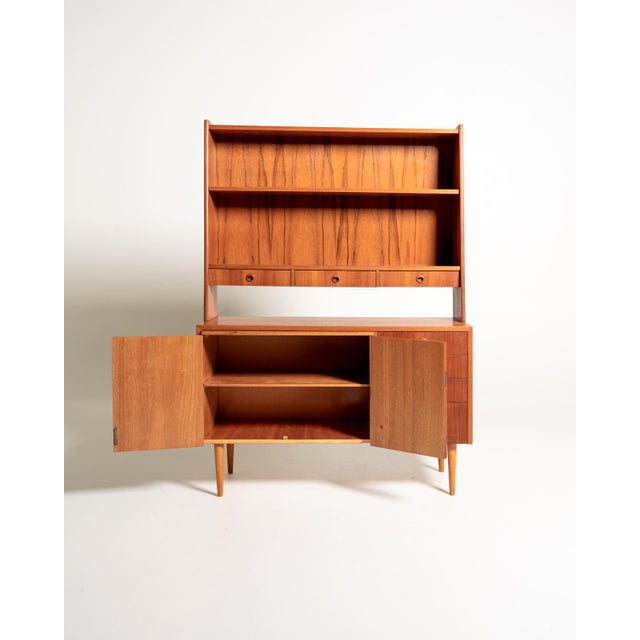 Teak bookcase with adjustable shelves, a pull-out writing surface, three small upper drawers, and a lower storage unit....