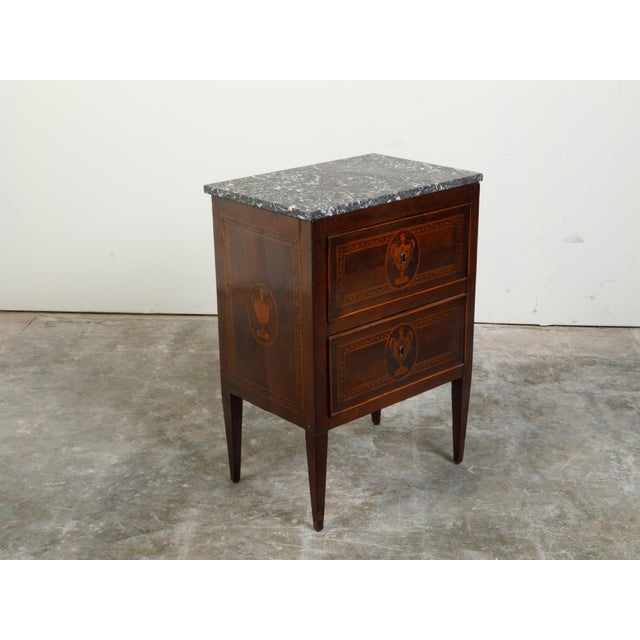 An Italian Neoclassical period walnut commode from the 18th century, with grey marble top and marquetry. Created in Italy...