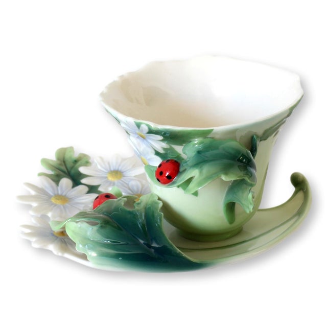 Franz porcelain cup and saucer set in the Ladybug pattern, featuring sculptural daisies, flowing foliage, and two vibrant...