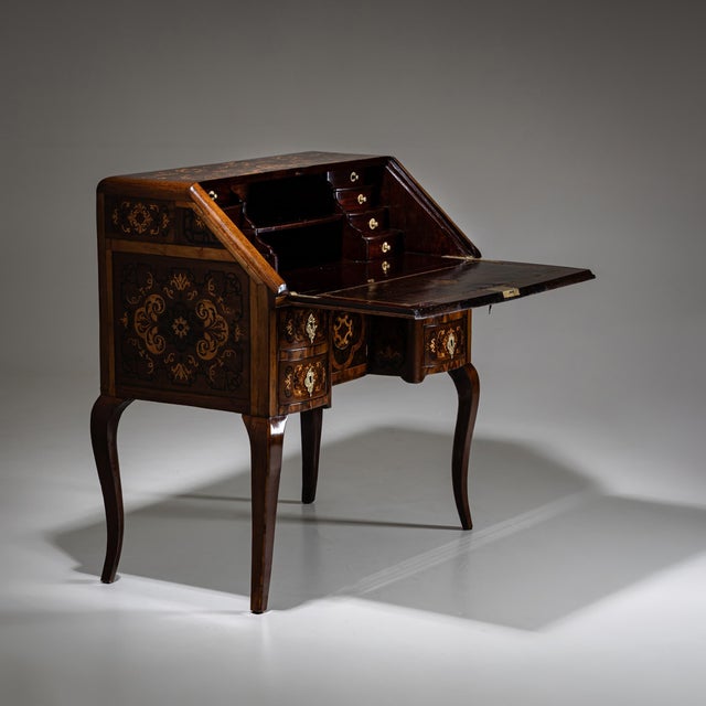 Small Baroque fall-front secretary on elegantly curved S-shaped legs, featuring four drawers and a central cabinet door....