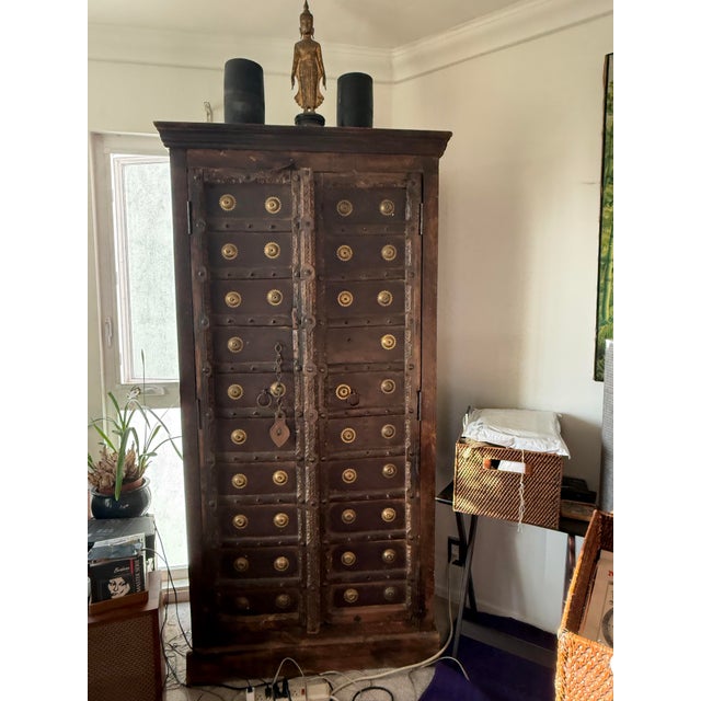 A tall wooden cabinet featuring two doors constructed from reclaimed architectural Indian panels, accented with rows of...