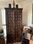 A tall wooden cabinet featuring two doors constructed from reclaimed architectural Indian panels, accented with rows of...