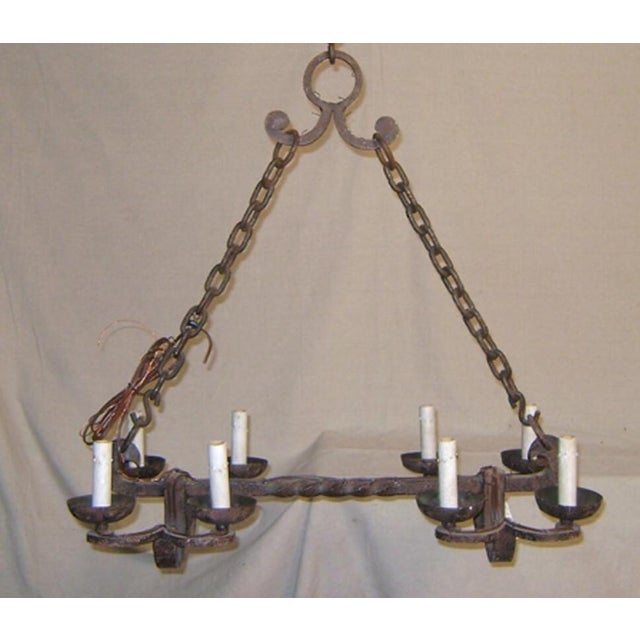 A robust eight-light iron chandelier. This single rod chandelier has a long thin twisting piece running along the bottom,...