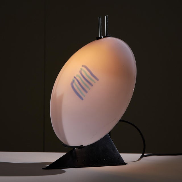 Italian postmodern table lamp, with a rhombus-shaped black metal base and two chrome stems holding the lamp. An abstract...