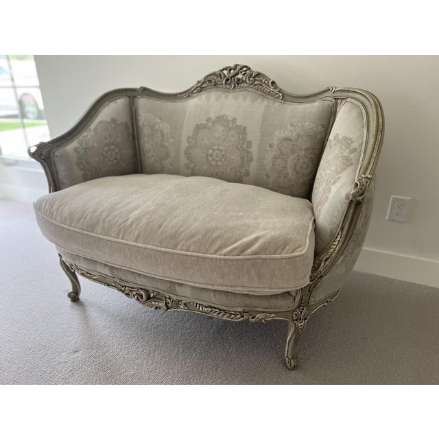 A beautiful vintage Louis XV style bergère settee featuring an intricately carved wood frame with a softly distressed...