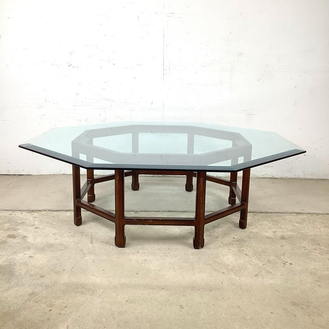 A striking vintage coffee table featuring a thick beveled hexagonal glass top resting on an architectural hardwood base...