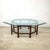 A striking vintage coffee table featuring a thick beveled hexagonal glass top resting on an architectural hardwood base...