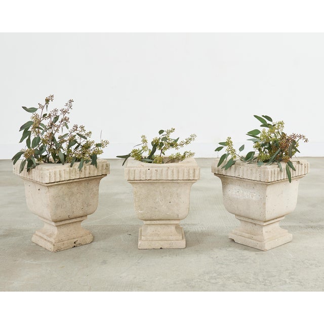 A sculptural set of three Italian molded stone urn planters or jardinieres executed in a warm ivory travertine tone. The...
