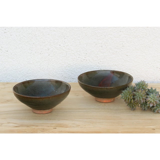 Two bowls, two different forms, joined by the same rich, dark iron glaze. The wider, shallower bowl carries warm rust and...