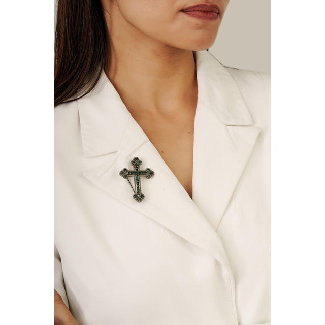 This Victorian style cross brooch pendant is crafted in 925 sterling silver, featuring vibrant round cut emeralds totaling...
