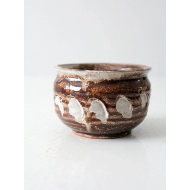 This is a vintage studio pottery bowl. The handmade cachepot features a warm brown glaze with white etched design.