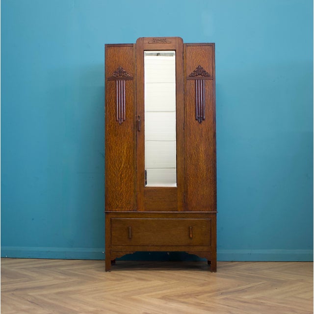 A 1930s oak wardrobe with a single mirrored door. The front features carved detailing and vertical reeded decoration...