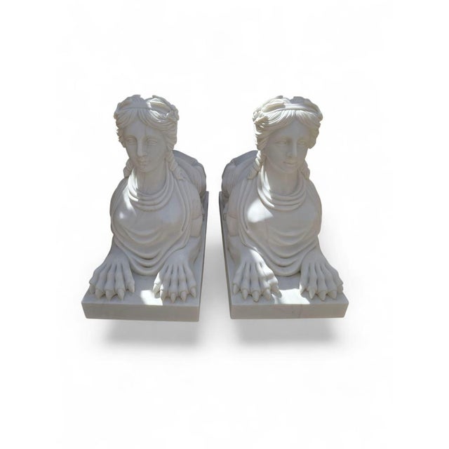 Elegant pair of Egyptian-style sphinx sculptures, hand-carved in white Italian marble during the 20th century. Each figure...