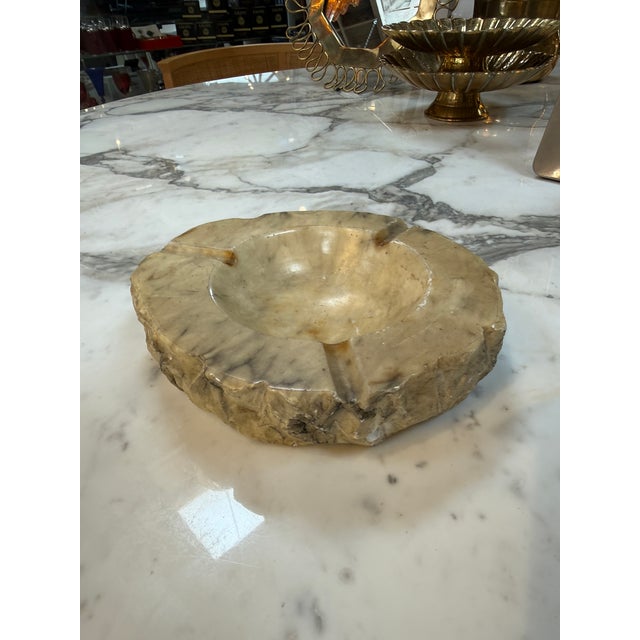 Solid marble ashtray featuring a polished bowl, multiple cigarette rests, and a rugged natural-stone exterior. Its warm...