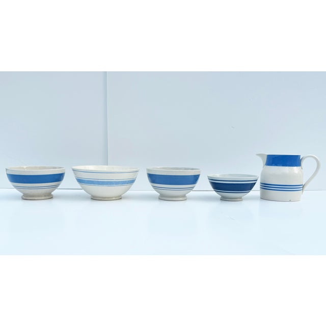 A lovely collection of English pottery, including four bowls and a pitcher, decorated with blue stripes on classic white...