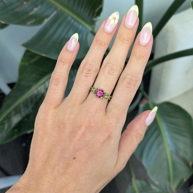 A stunning 1.1Ct purple sapphire takes center stage, accented by vibrant natural tsavorites for a rich, elegant contrast....