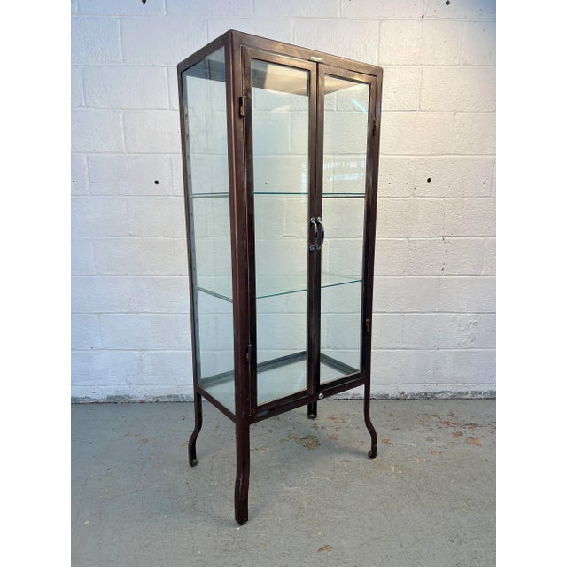 A sleek glass and metal cabinet by Dulton Co., featuring glass shelves and original hardware. Its clean industrial design...